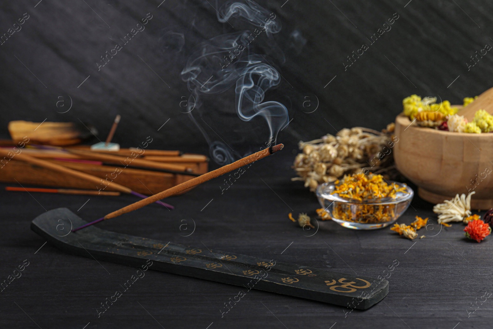 Photo of Aromatic incense stick smoldering in holder with om sign on black table