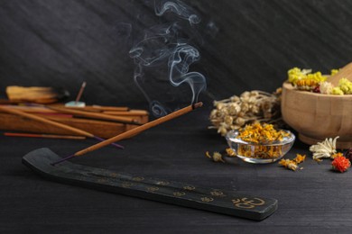 Photo of Aromatic incense stick smoldering in holder with om sign on black table