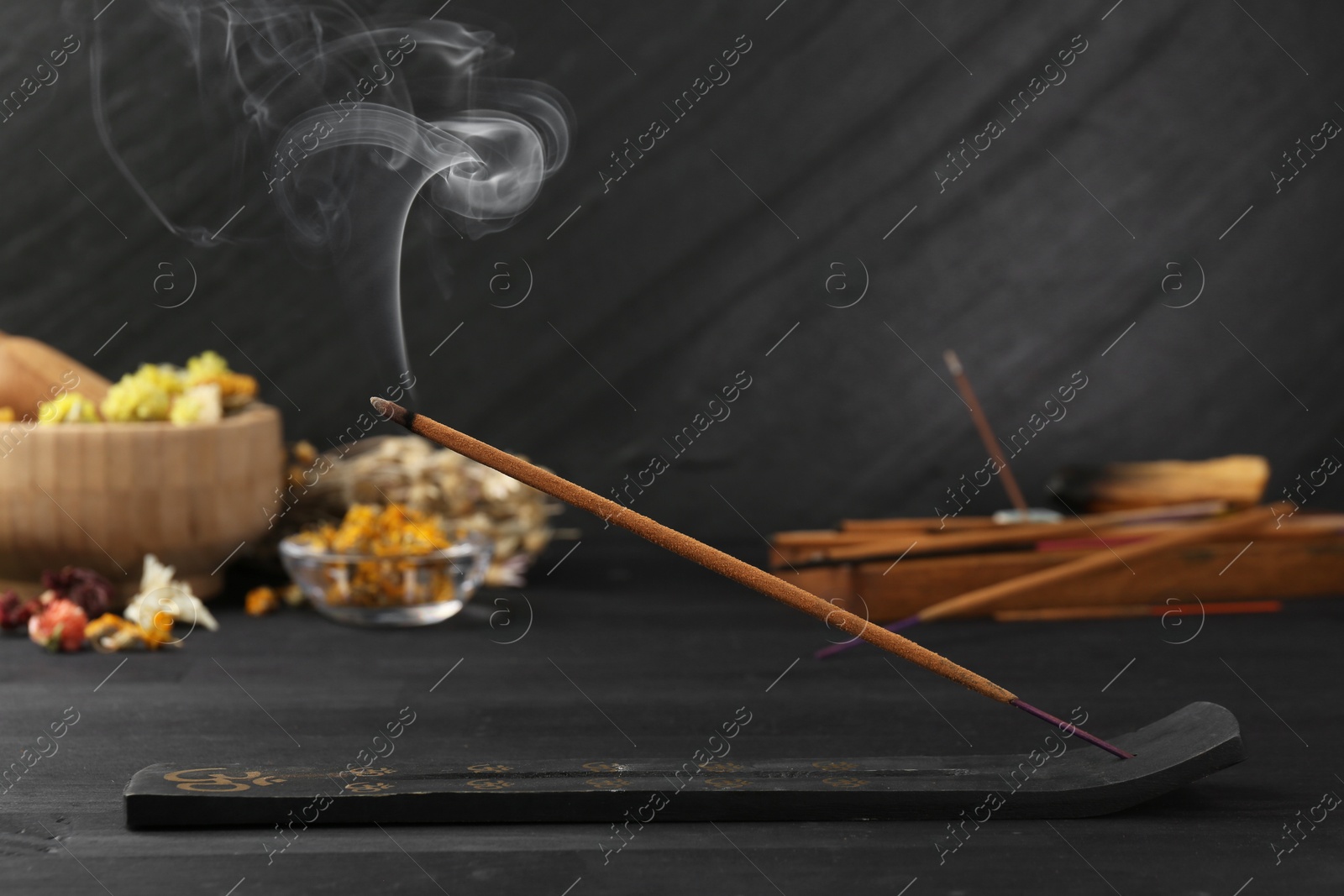 Photo of Aromatic incense stick smoldering in holder with om sign on black table
