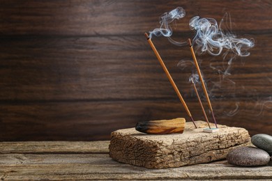 Aromatic incense sticks smoldering on wooden table. Space for text