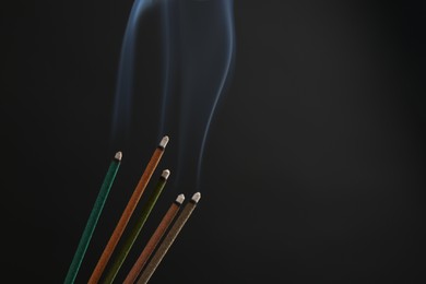 Photo of Aromatic incense sticks smoldering on black background. Space for text