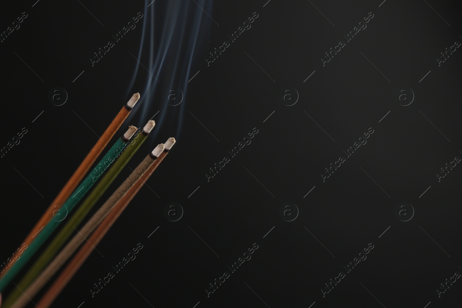 Photo of Aromatic incense sticks smoldering on black background. Space for text