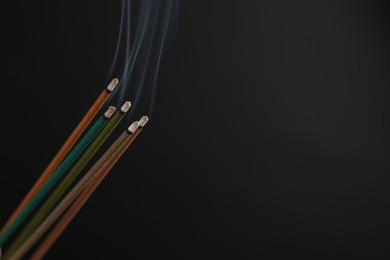 Photo of Aromatic incense sticks smoldering on black background. Space for text