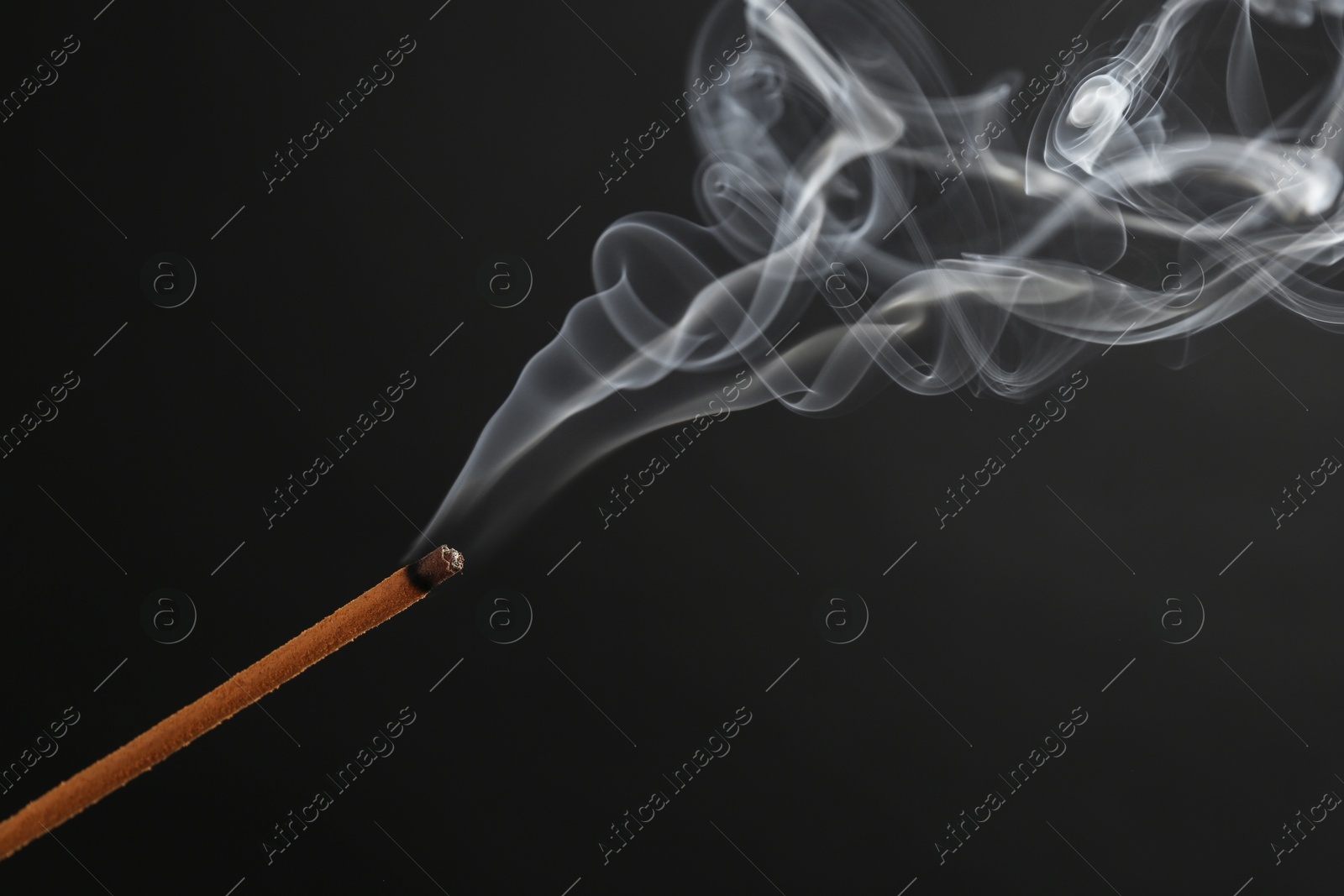 Photo of Aromatic incense stick smoldering on black background, closeup