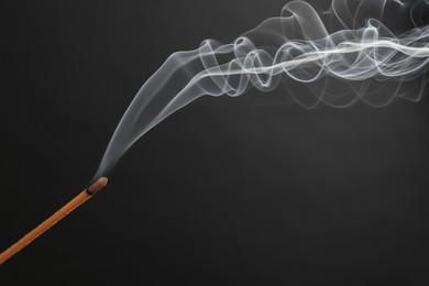Photo of Aromatic incense stick smoldering on black background, closeup