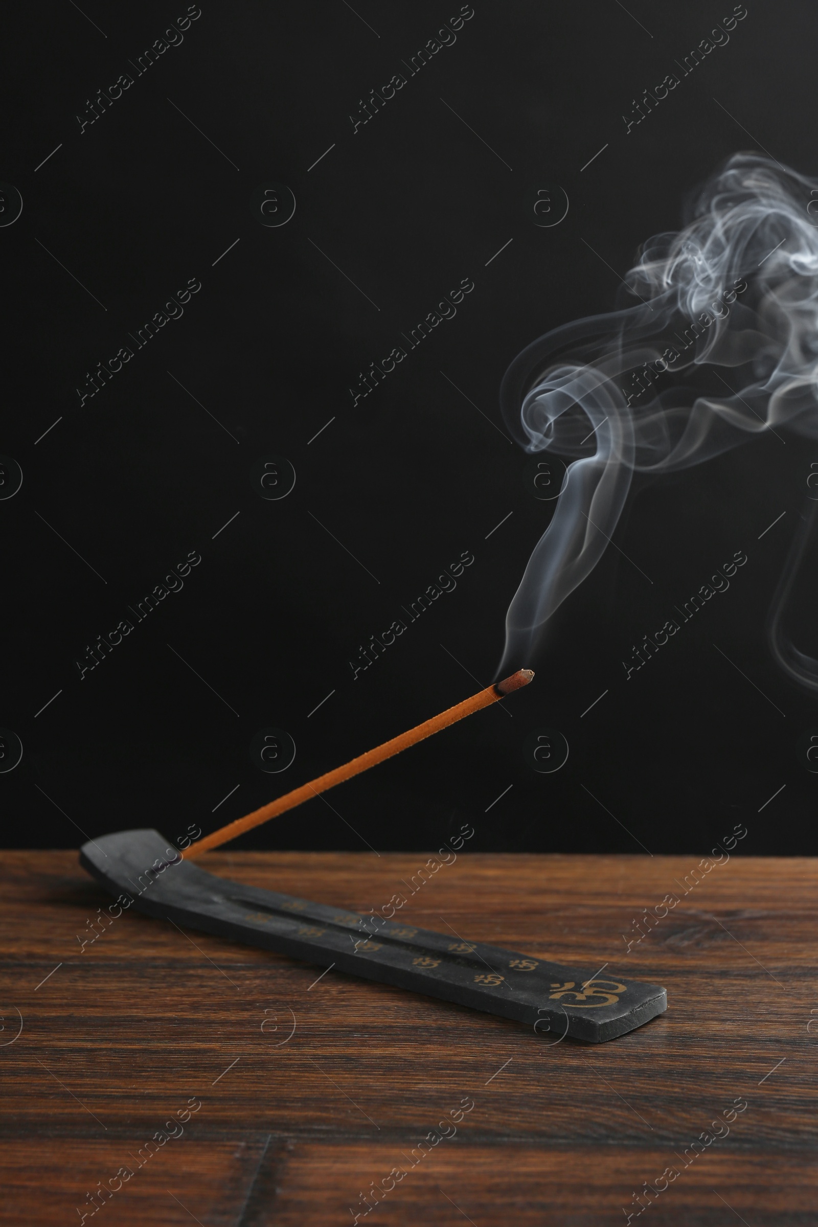 Photo of Aromatic incense stick smoldering in holder with Om signs on wooden table