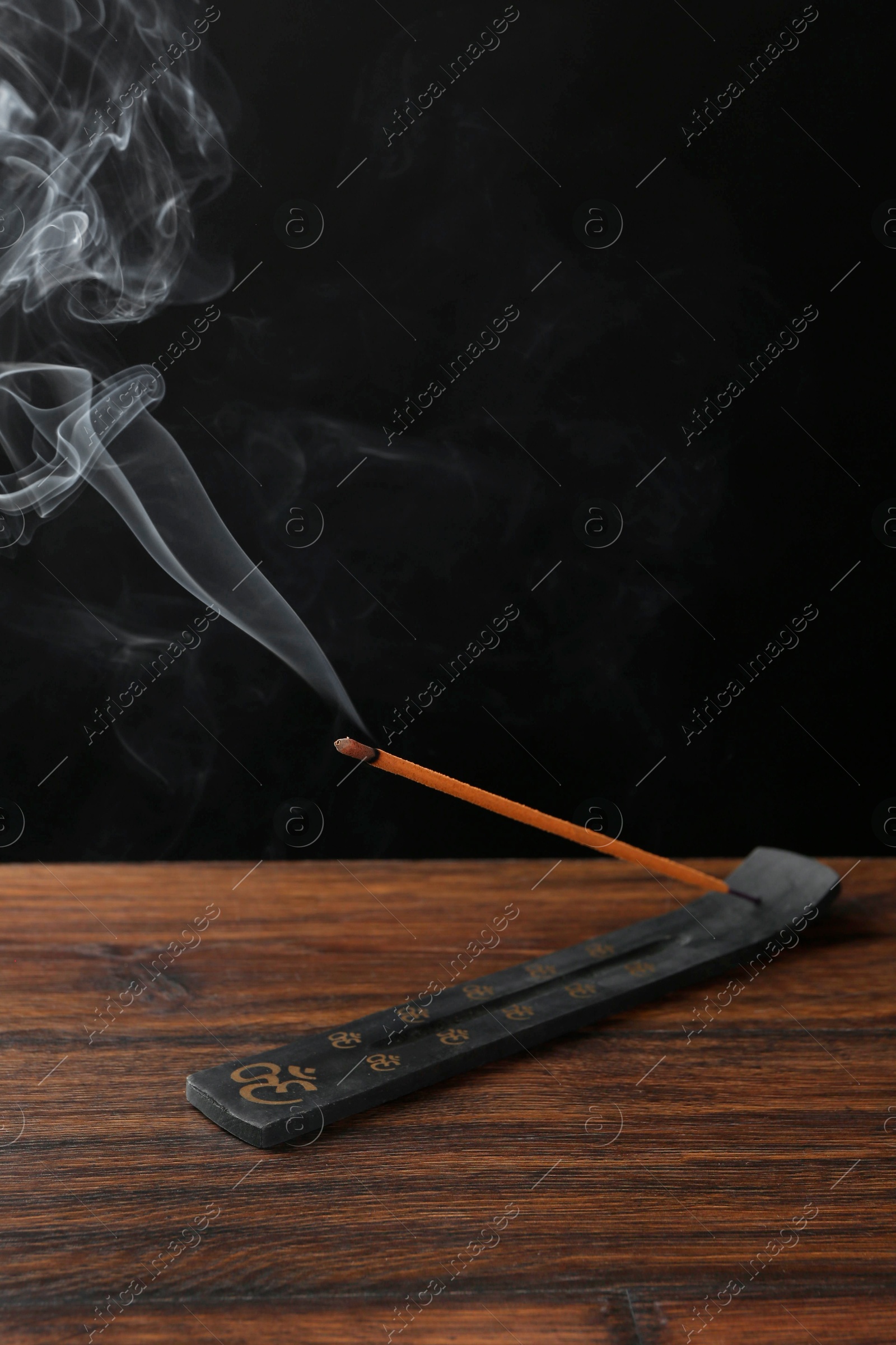 Photo of Aromatic incense stick smoldering in holder with Om signs on wooden table