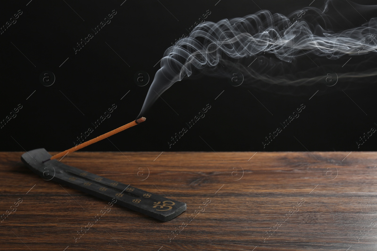 Photo of Aromatic incense stick smoldering in holder with Om signs on wooden table