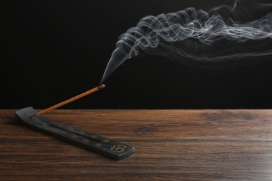 Aromatic incense stick smoldering in holder with Om signs on wooden table