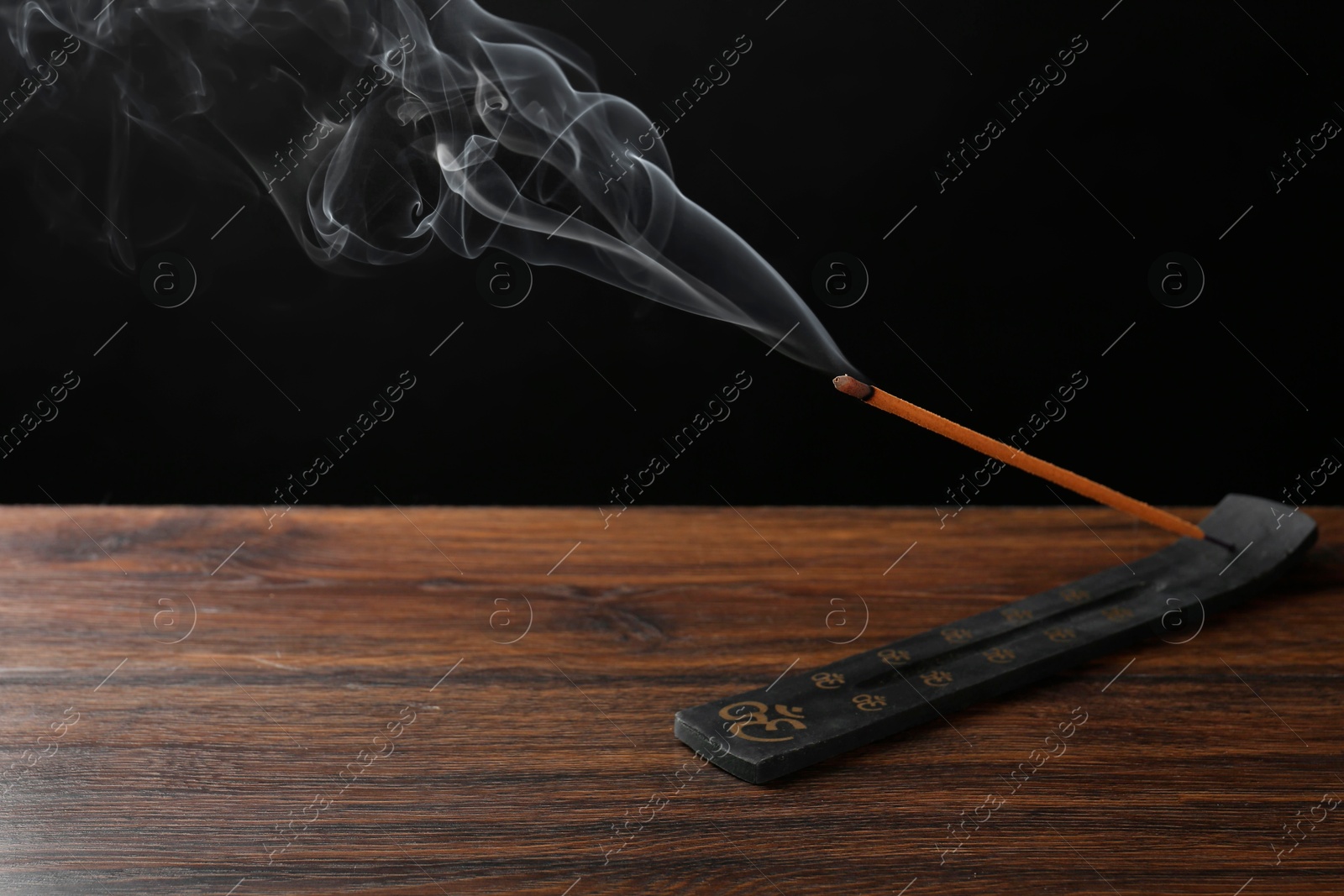 Photo of Aromatic incense stick smoldering in holder with Om signs on wooden table