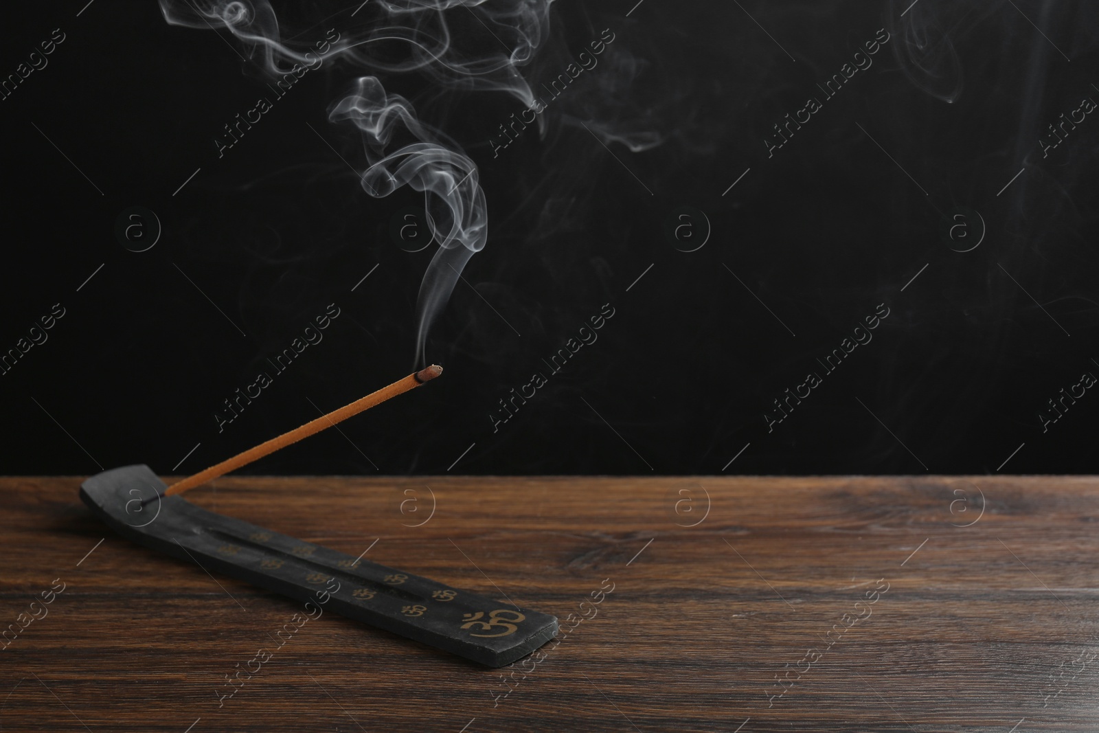 Photo of Aromatic incense stick smoldering in holder with Om signs on wooden table. Space for text