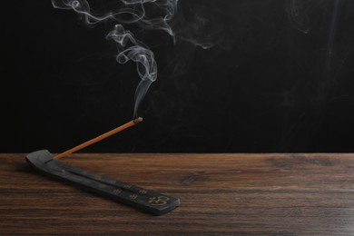 Photo of Aromatic incense stick smoldering in holder with Om signs on wooden table. Space for text