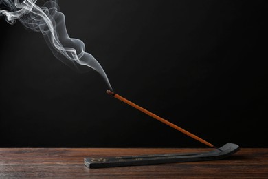 Photo of Aromatic incense stick smoldering in holder with Om signs on wooden table