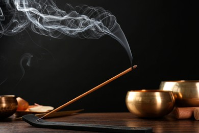 Aromatic incense stick smoldering in holder with Om signs on wooden table