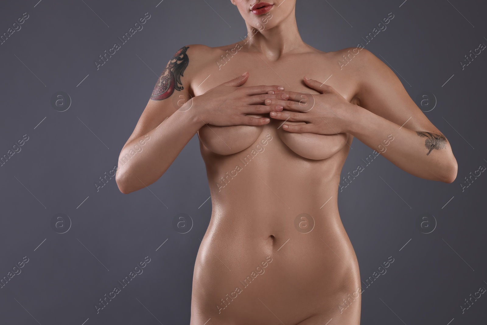 Photo of Nude woman with tattoos on grey background, closeup