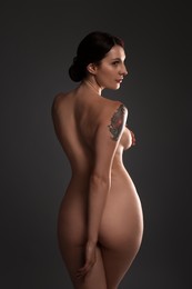 Photo of Beautiful nude woman with tattoo posing on dark background, back view