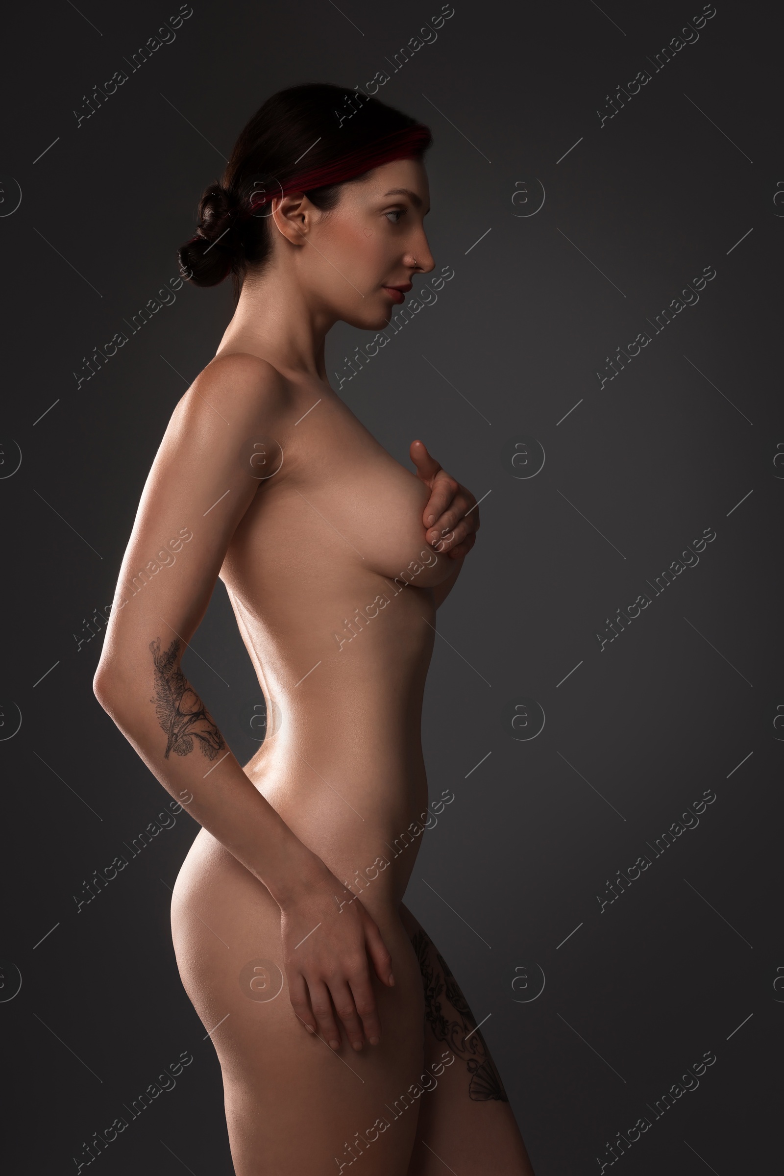 Photo of Beautiful nude woman with tattoos posing on dark background