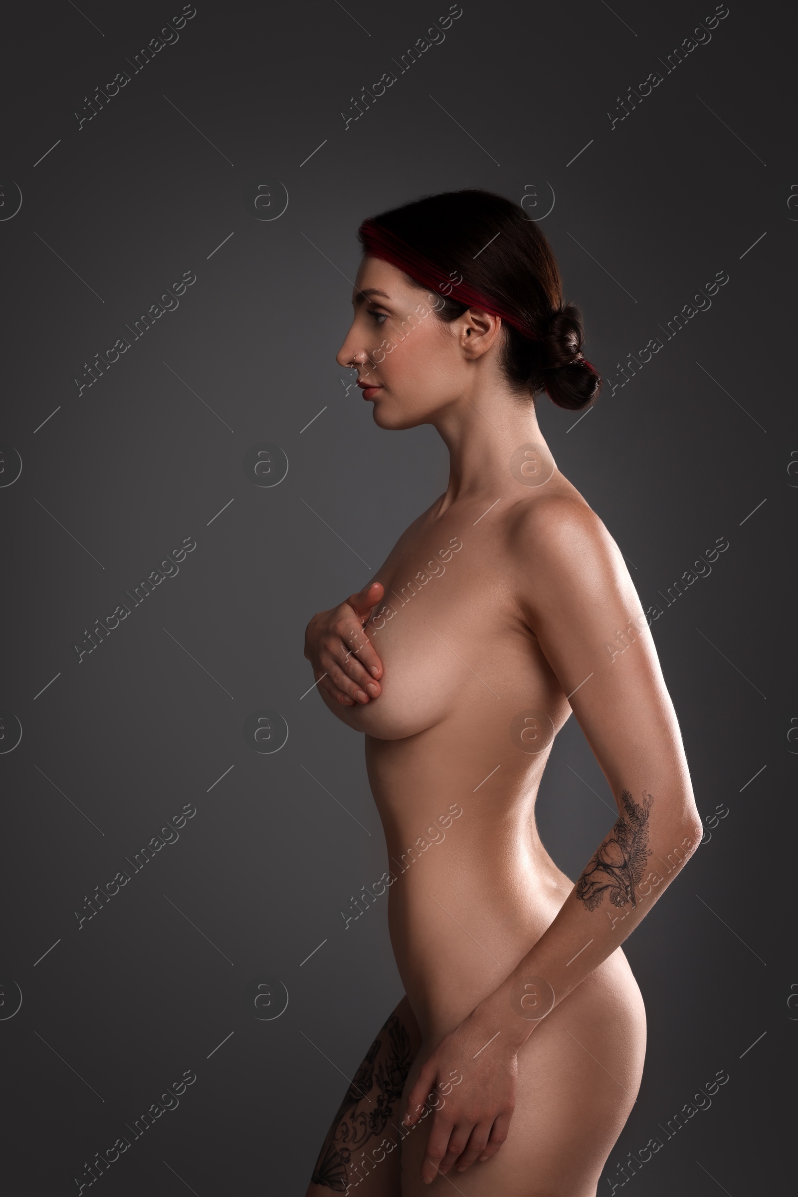 Photo of Beautiful nude woman with tattoos posing on dark background