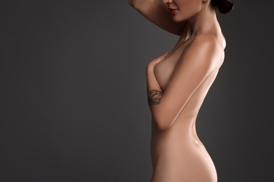 Photo of Nude woman with tattoo posing on dark background, closeup. Space for text