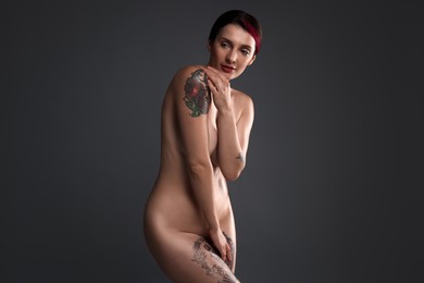 Photo of Beautiful nude woman with tattoo posing on dark background