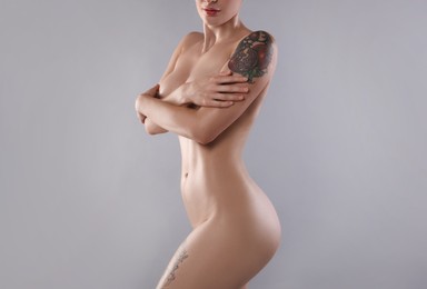 Nude woman with tattoo on light grey background, closeup. Space for text