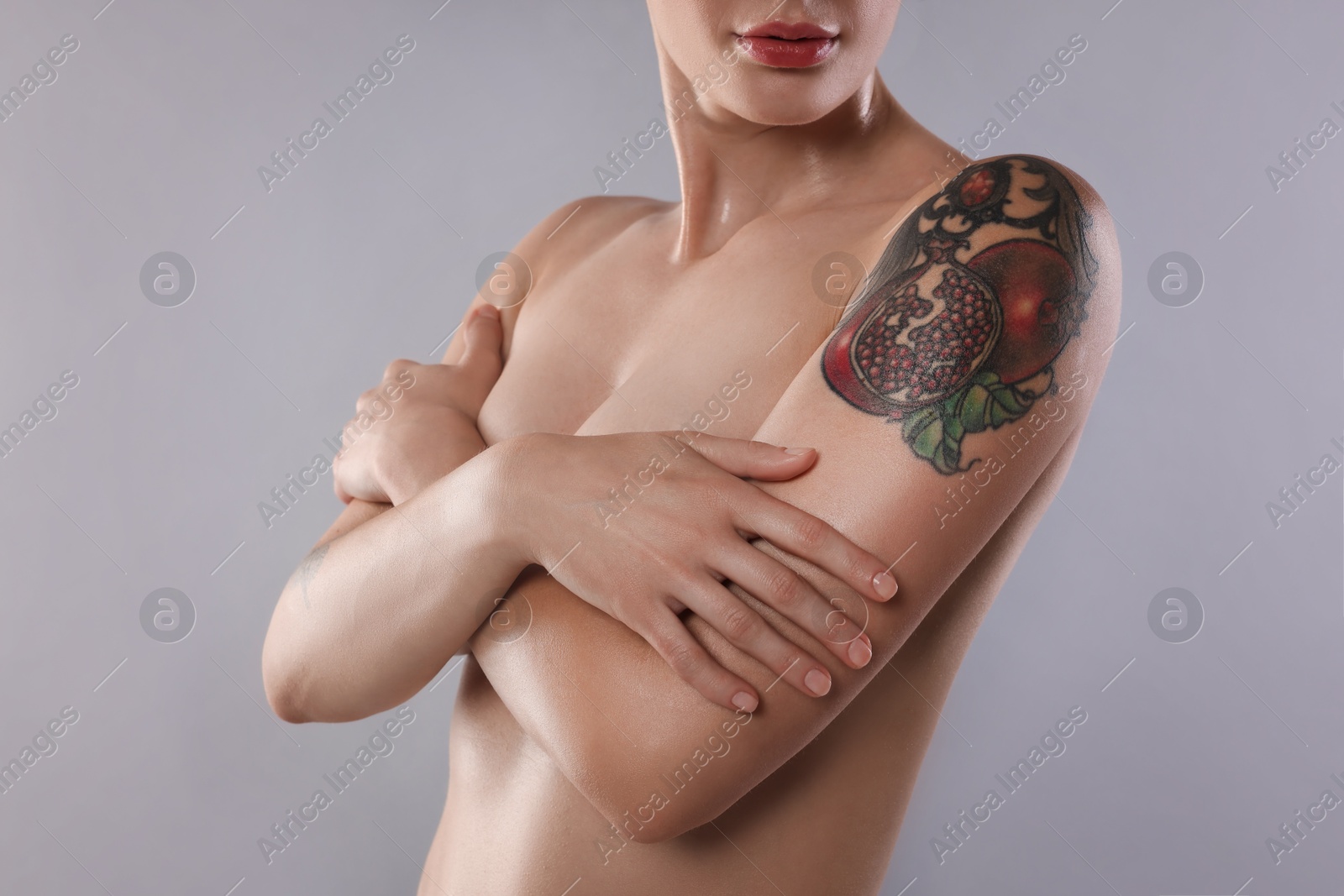 Photo of Nude woman with tattoo on light grey background, closeup