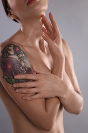 Photo of Nude woman with tattoo on light grey background, closeup