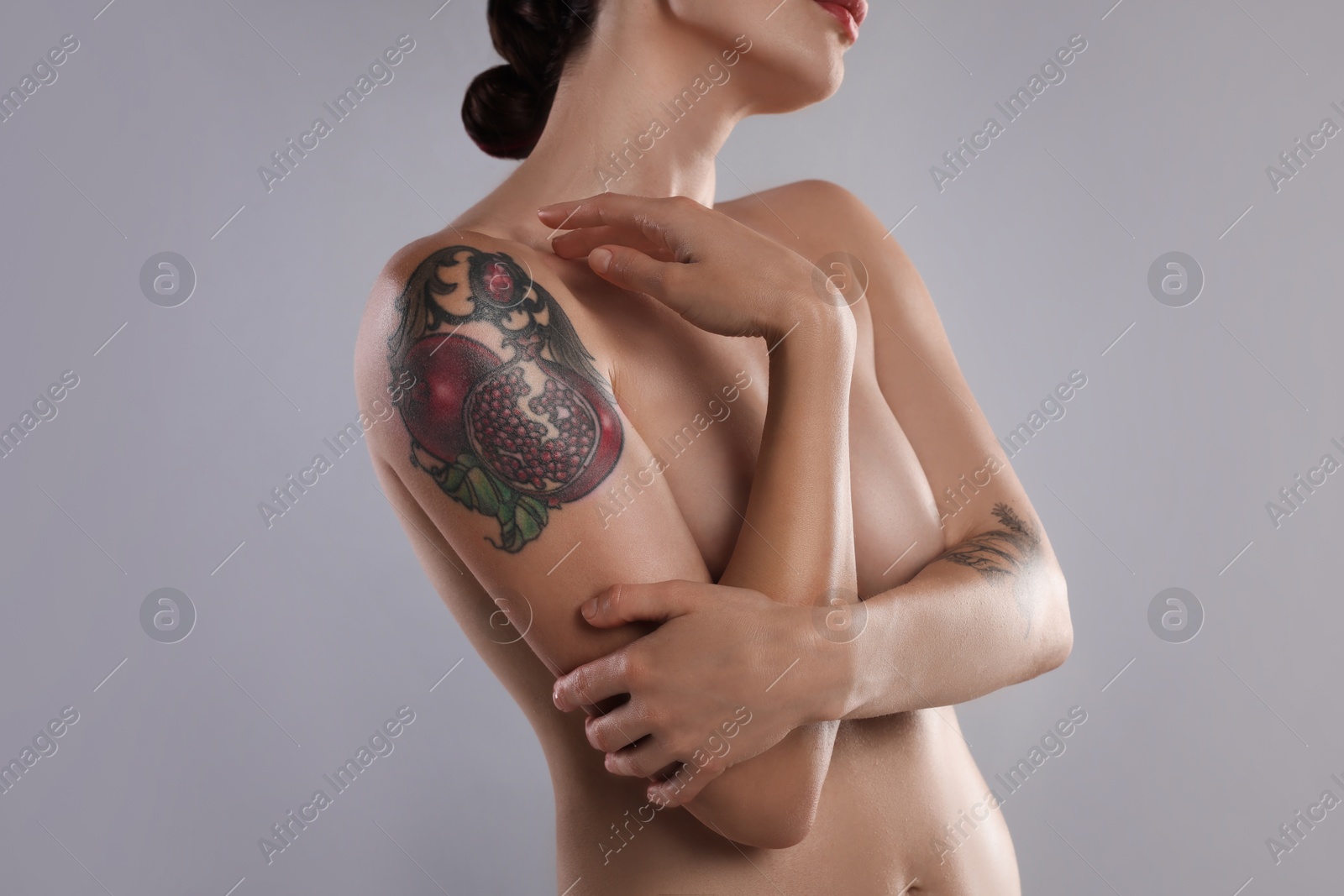 Photo of Nude woman with tattoo on light grey background, closeup