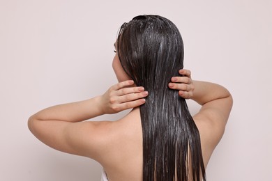 Photo of Woman applying hair mask on light background, back view