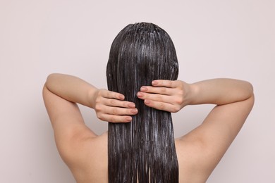 Woman applying hair mask on light background, back view