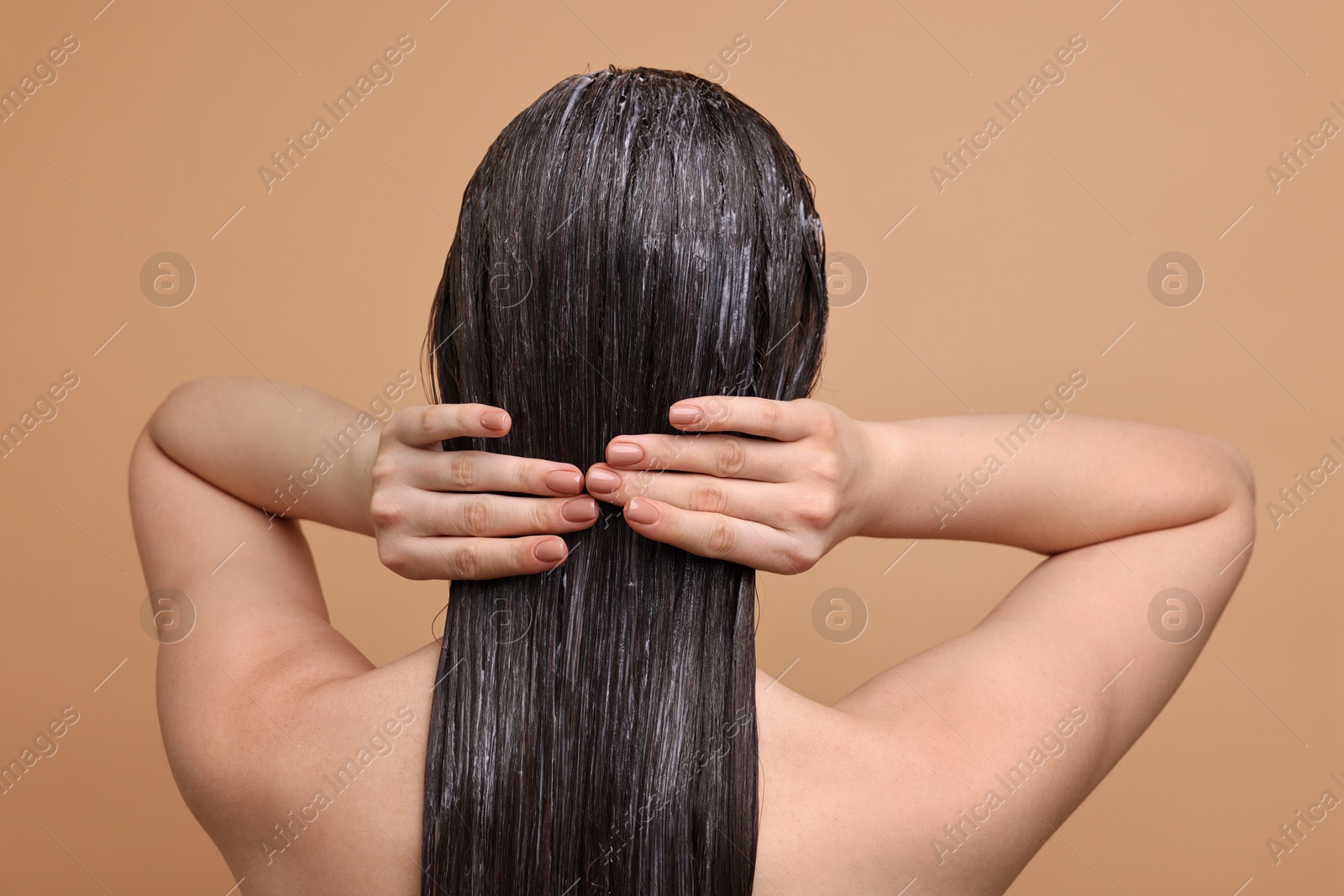 Photo of Woman applying hair mask on beige background, back view