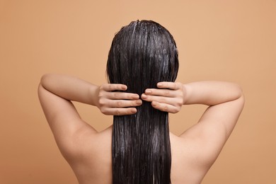 Photo of Woman applying hair mask on beige background, back view