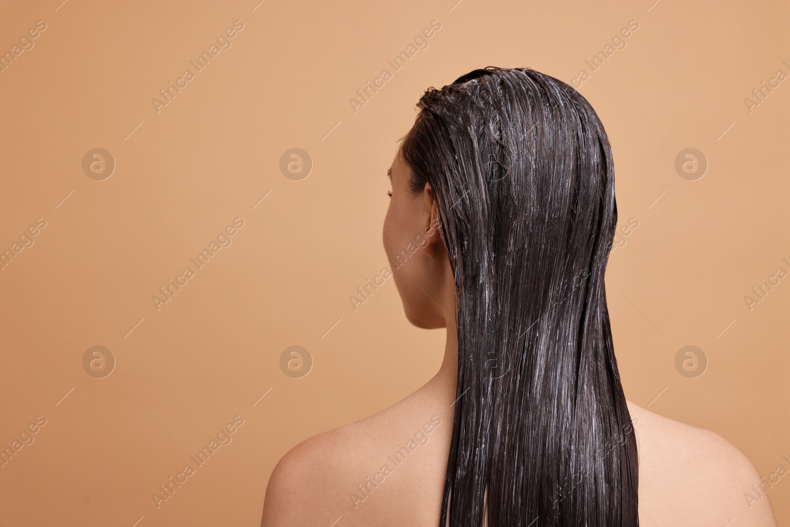 Photo of Woman with applied hair mask on beige background, back view. Space for text