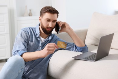 Photo of Online banking. Young man with credit card talking by smartphone at home