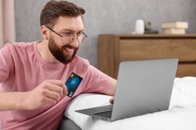 Photo of Online banking. Happy young man with credit card and laptop paying purchase at home