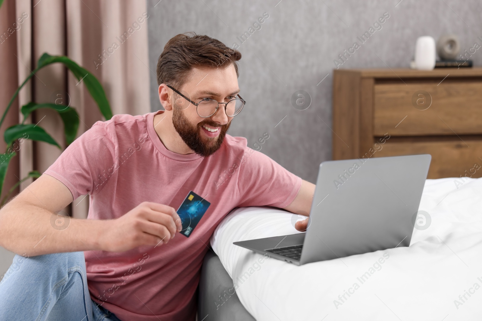 Photo of Online banking. Happy young man with credit card and laptop paying purchase at home