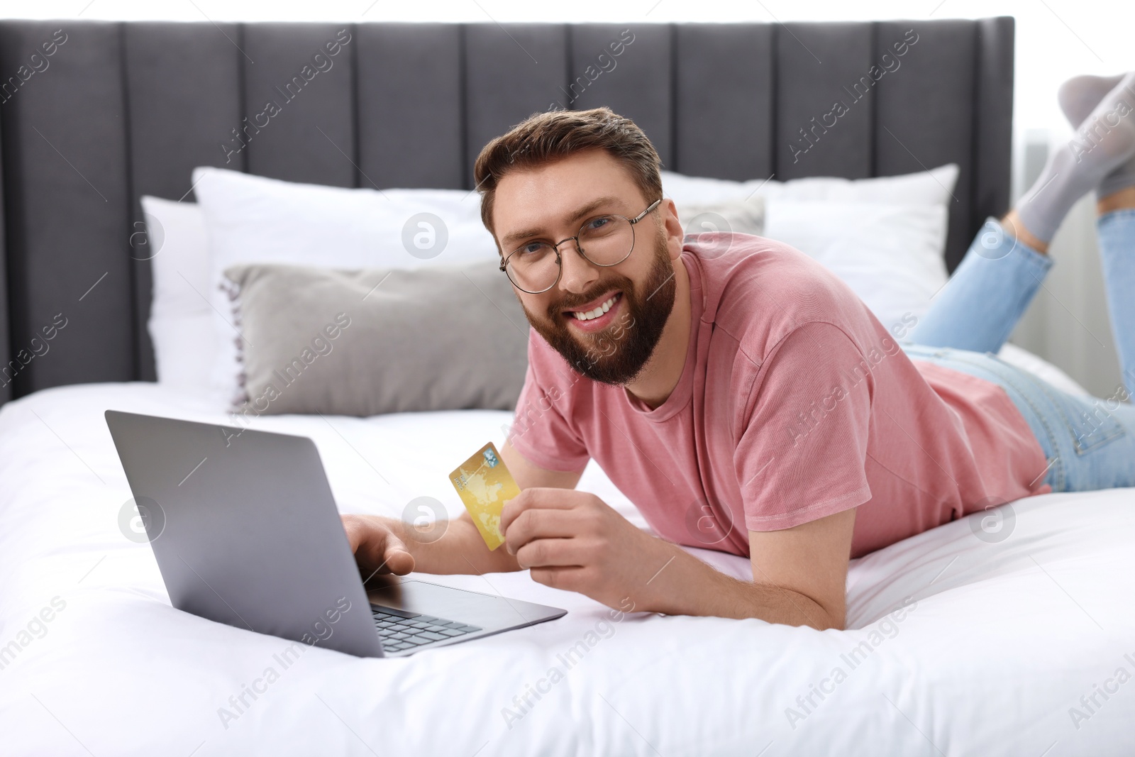 Photo of Online banking. Happy young man with credit card and laptop paying purchase at home