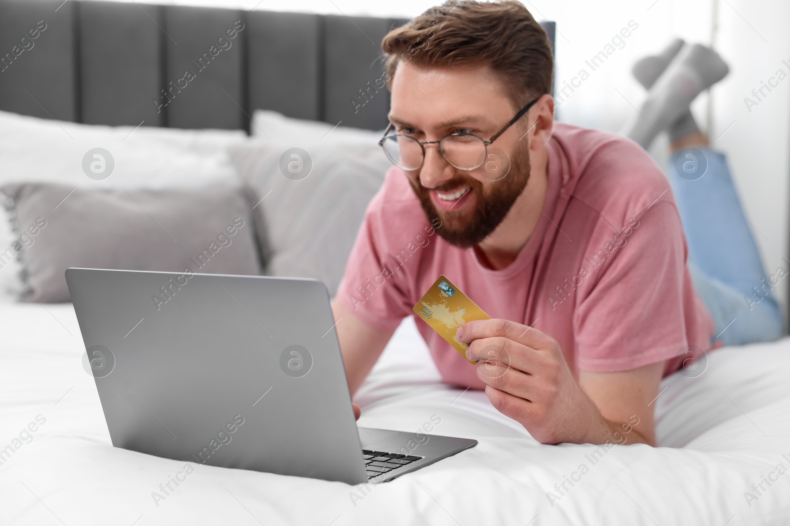 Photo of Online banking. Happy young man with credit card and laptop paying purchase at home