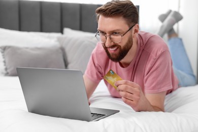 Photo of Online banking. Happy young man with credit card and laptop paying purchase at home