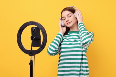 Photo of Technology blogger reviewing headphones and recording video with smartphone and ring lamp on orange background