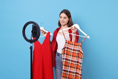 Photo of Fashion blogger reviewing dresses and recording video with smartphone and ring lamp on light blue background