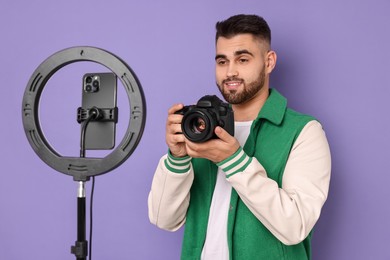 Technology blogger reviewing camera and recording video with smartphone and ring lamp on purple background