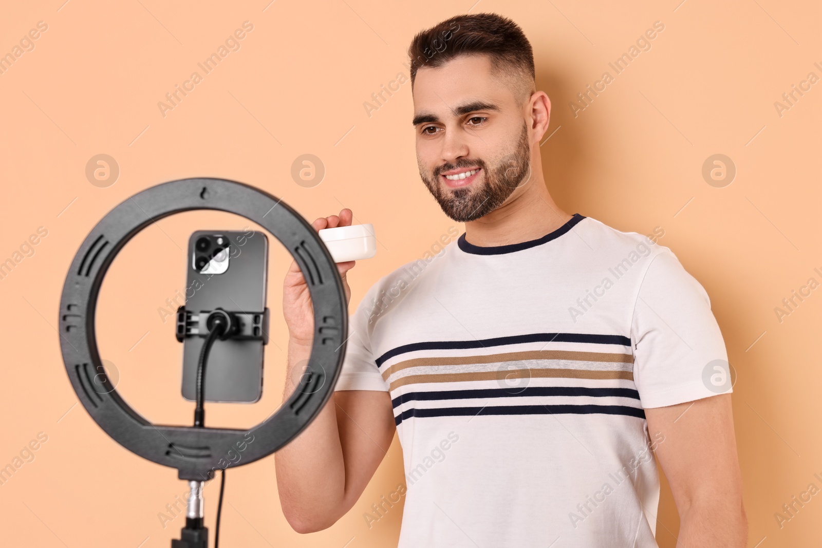 Photo of Beauty blogger reviewing cosmetic product and recording video with smartphone and ring lamp on beige background