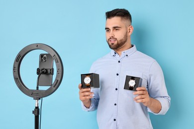 Photo of Fashion blogger reviewing watches and recording video with smartphone and ring lamp on light blue background