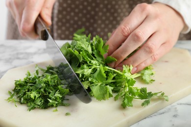 Woman cutting fresh coriander at white marble table, closeup