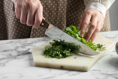 Photo of Woman cutting fresh coriander at white marble table, closeup