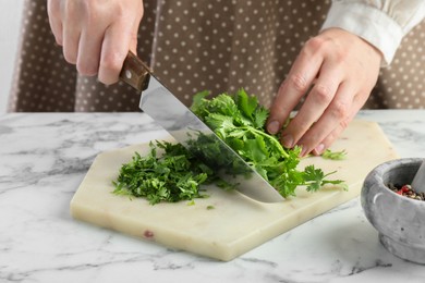 Photo of Woman cutting fresh coriander at white marble table, closeup