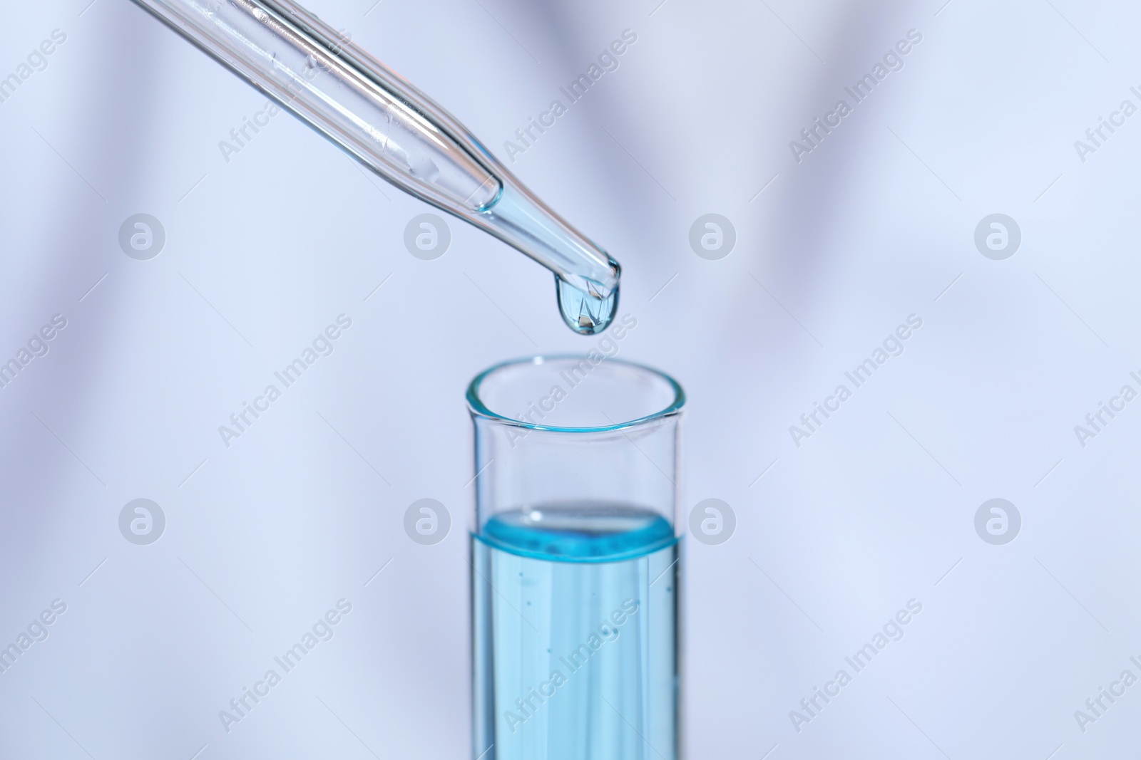 Photo of Dripping liquid from pipette into test tube on blurred background, closeup