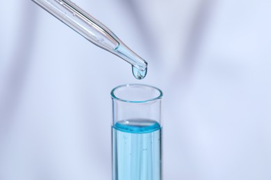 Dripping liquid from pipette into test tube on blurred background, closeup