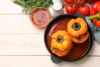 Photo of Tasty stuffed peppers in pan, sauce and products on light wooden table, flat lay. Space for text